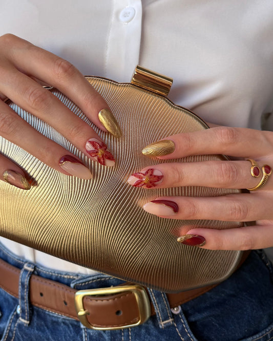set de uñas press-on otoñal dorado y rojo burdeos con ojo de gato, cromático y flor 3D cogiendo un bolso de fiesta dorado