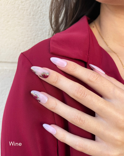 una mano con uñas press-on nudes con flores  en color vino y contorno dorado cromático y camisa burdeos