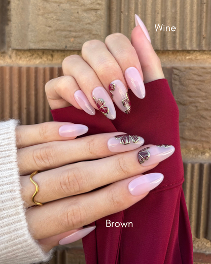 con uñas press-on puestas nudes con flores combinables en color marrón y vino y contorno dorado cromático una mano de cada color