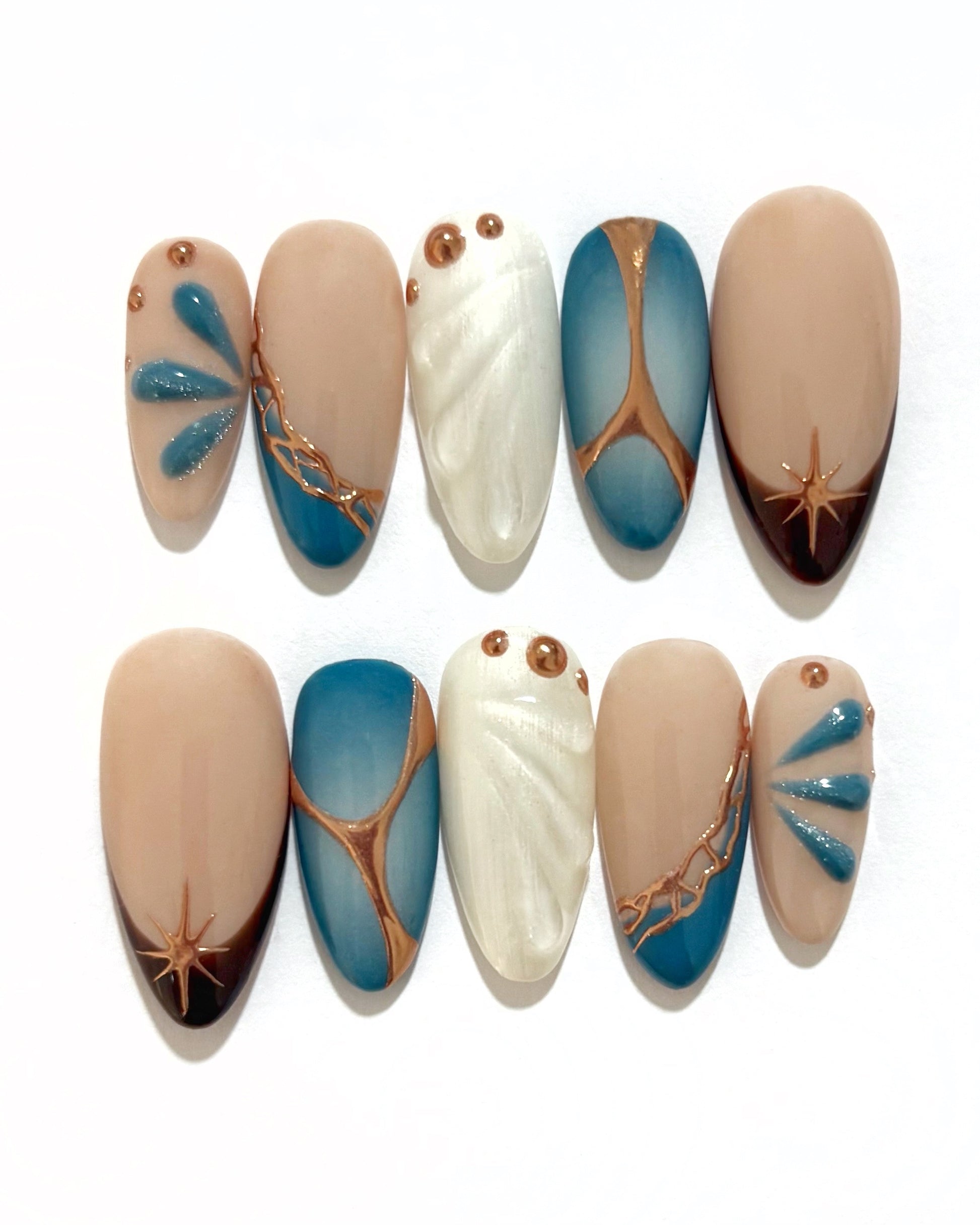 set de uñas press-on azul con toques de cobre cromático, degradado con aerógrafo, blanco perlado con gotas de gel 3D, ojo de gato y estrella