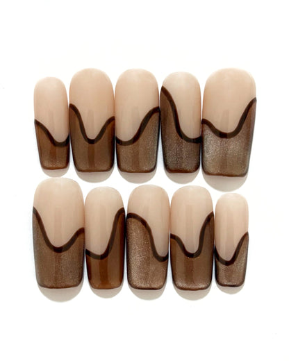 set de uñas press-on nude con francesa abstracta de color marrón con efecto ojo de gato y un línea delgada marrón que separa la francesa