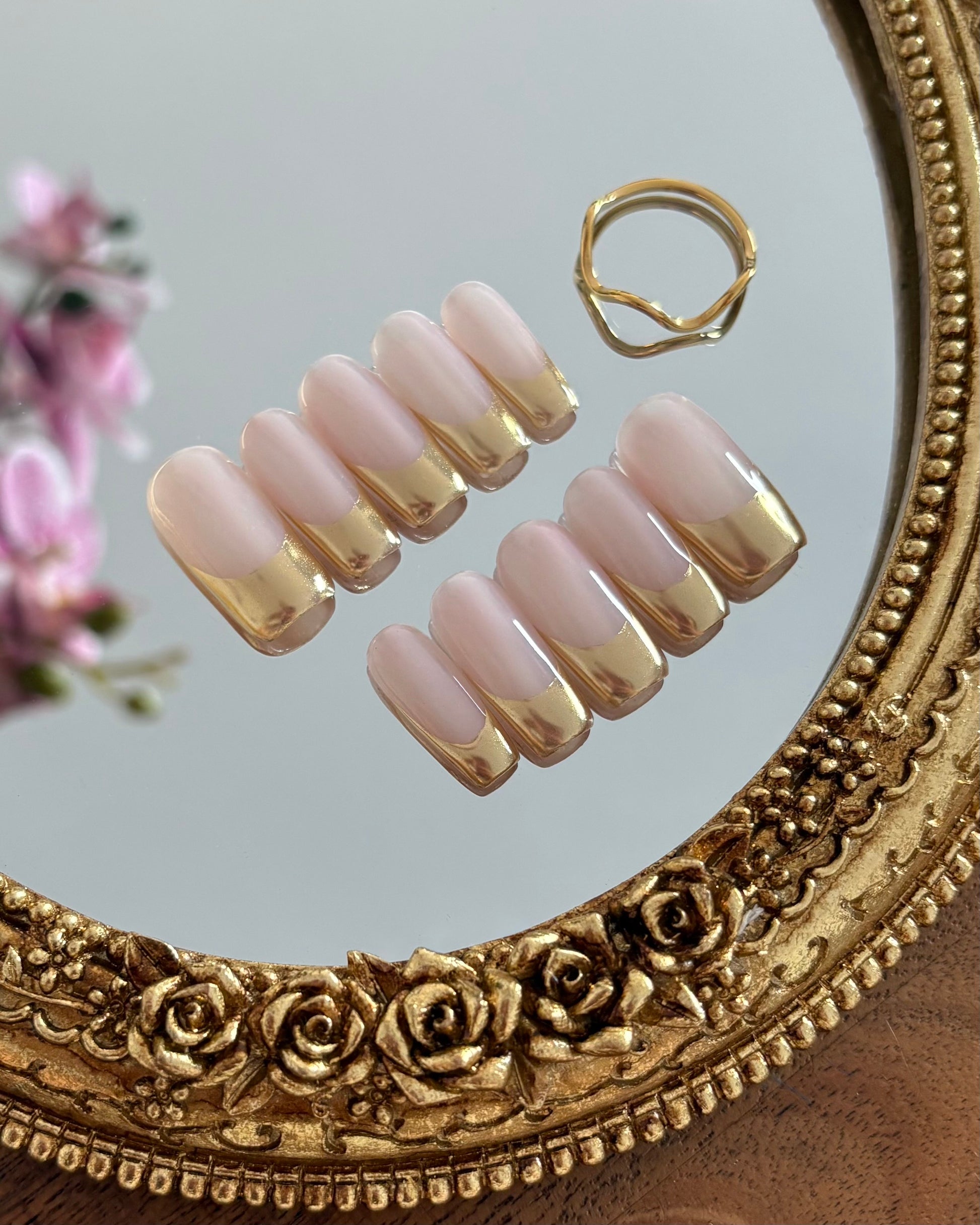 set de uñas press-on nudes con francesa cromática dorada apoyadas sobre un espejo rollo antiguo dorado 
