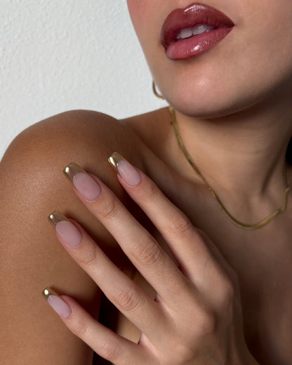 set de uñas press-on nudes con francesa cromática dorada apoyando sobre el brazo con labio pintado 