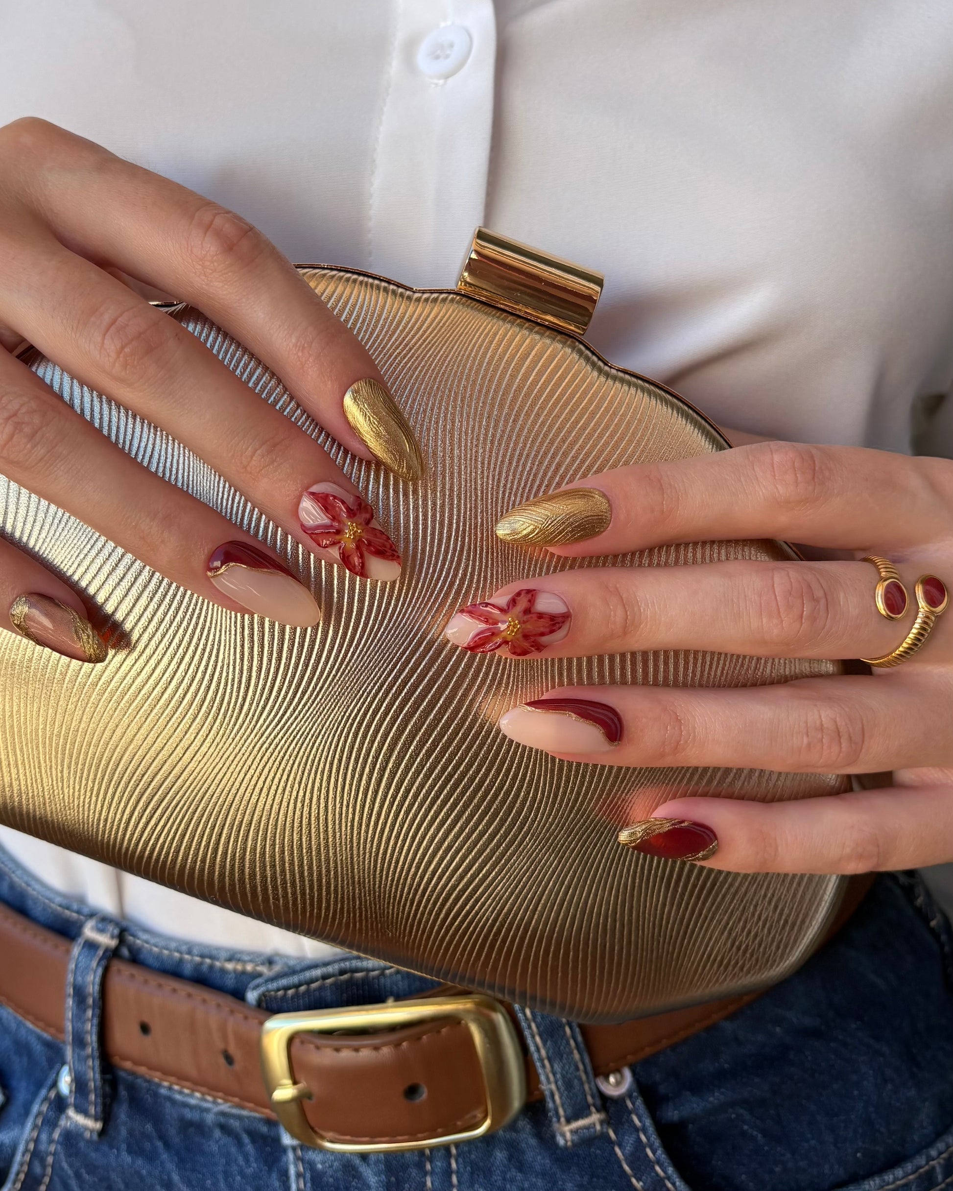 set de uñas press-on otoñal dorado y rojo burdeos con ojo de gato, cromático y flor 3D cogiendo un bolso de fiesta dorado