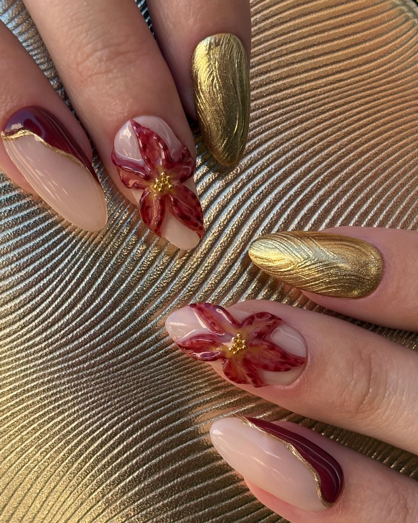 set de uñas press-on otoñal dorado y rojo burdeos con ojo de gato, cromático y flor 3D plano de cerca con fondo dorado