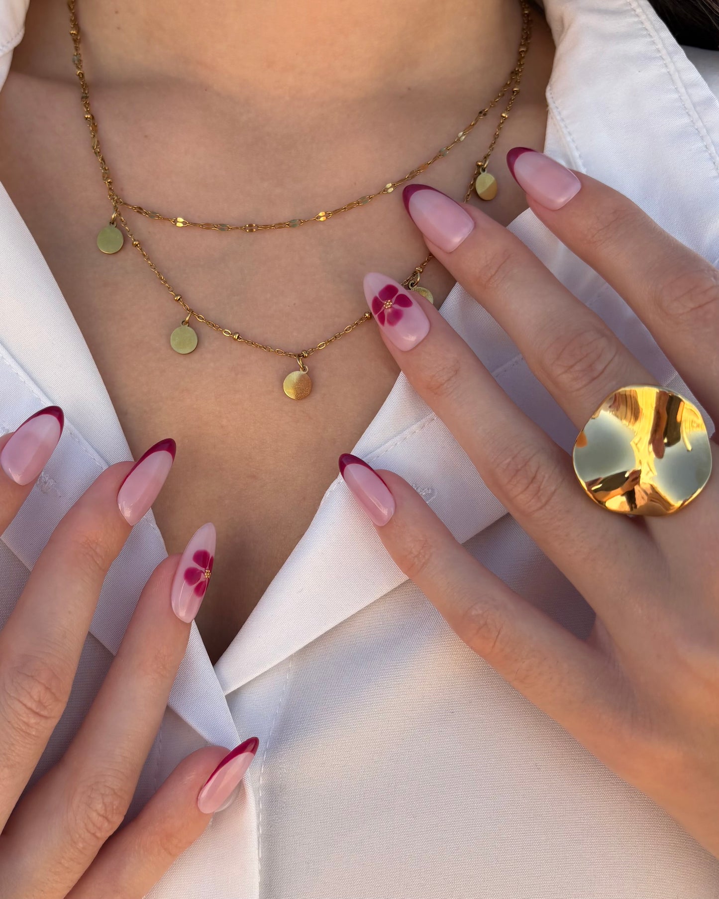 set de uñas press-on nudes con francesa burdeos y flor blooming con caviar dorado tocando cuello con anillo y collar