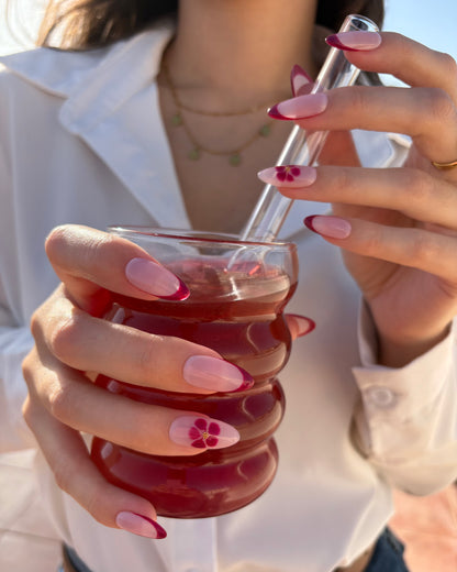 set de uñas press-on nudes con francesa burdeos y flor blooming con caviar dorado tocando pajita de un bubble tea