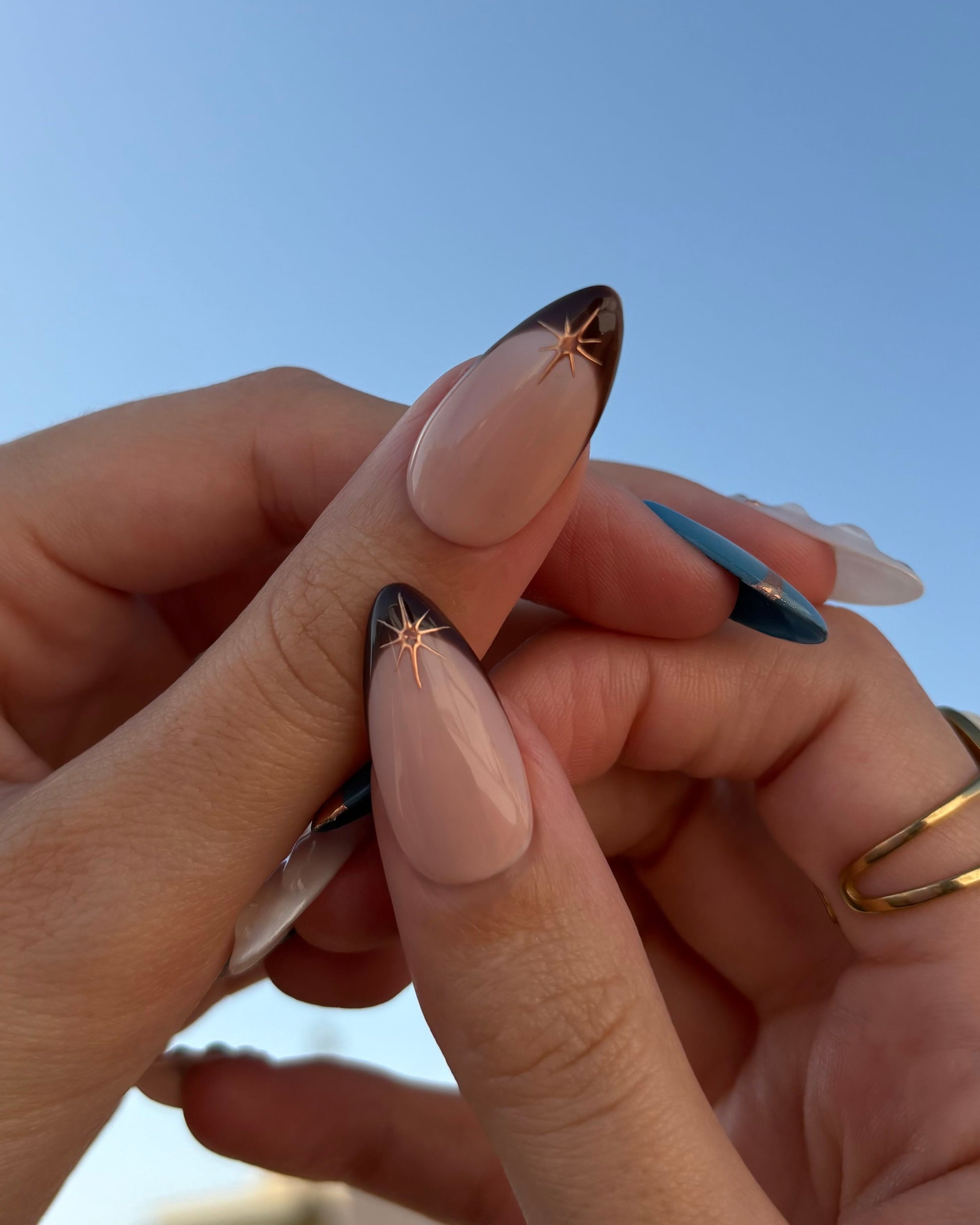 set de uñas press-on azul con toques de cobre cromático, degradado con aerógrafo, blanco perlado con gotas de gel 3D, ojo de gato y estrella vista de los pulgares francesa marrón