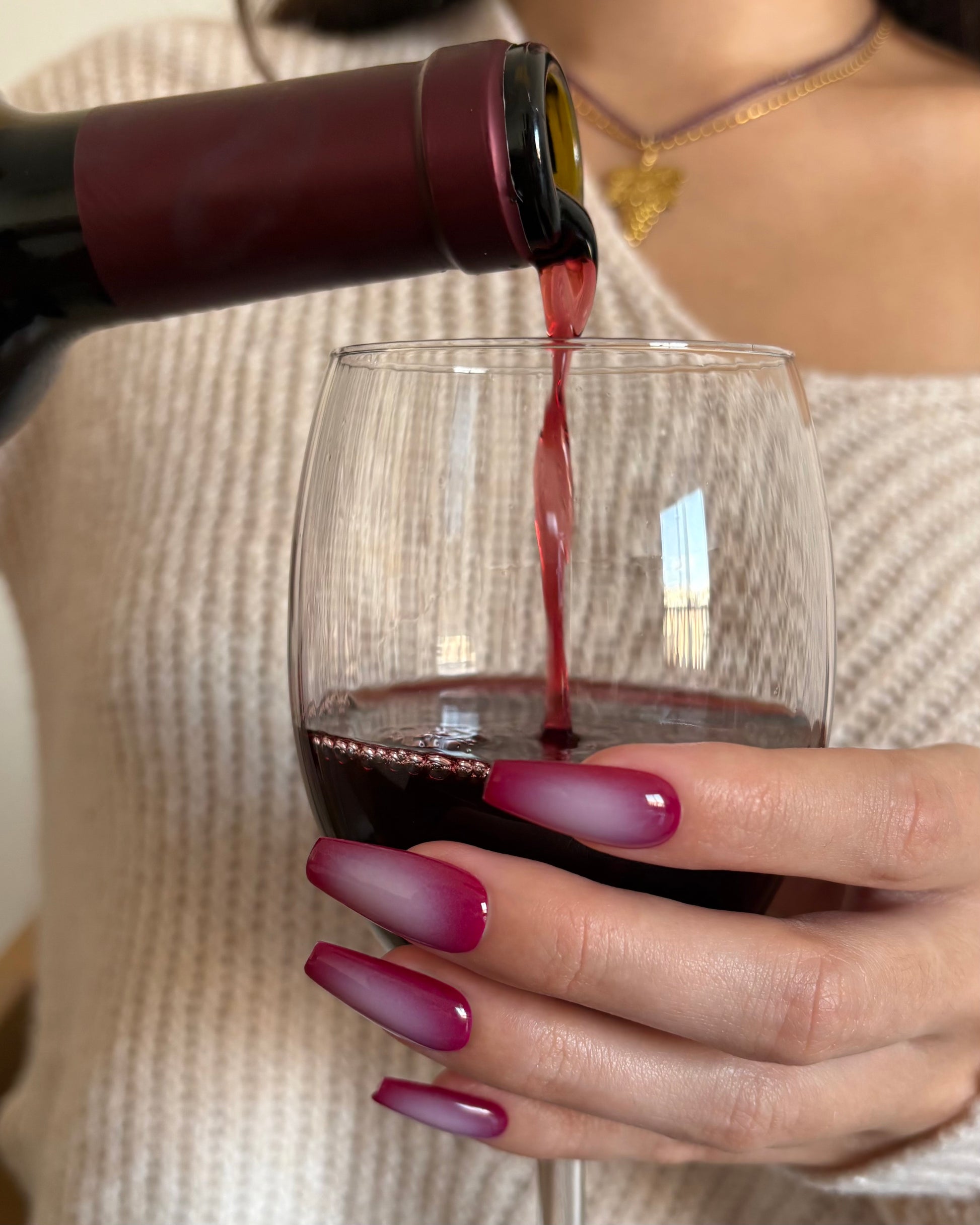 set de uñas press-on burdeos con degradado aura en el centro de color beige hecho con aerógrafo sirviendo una copa de vino