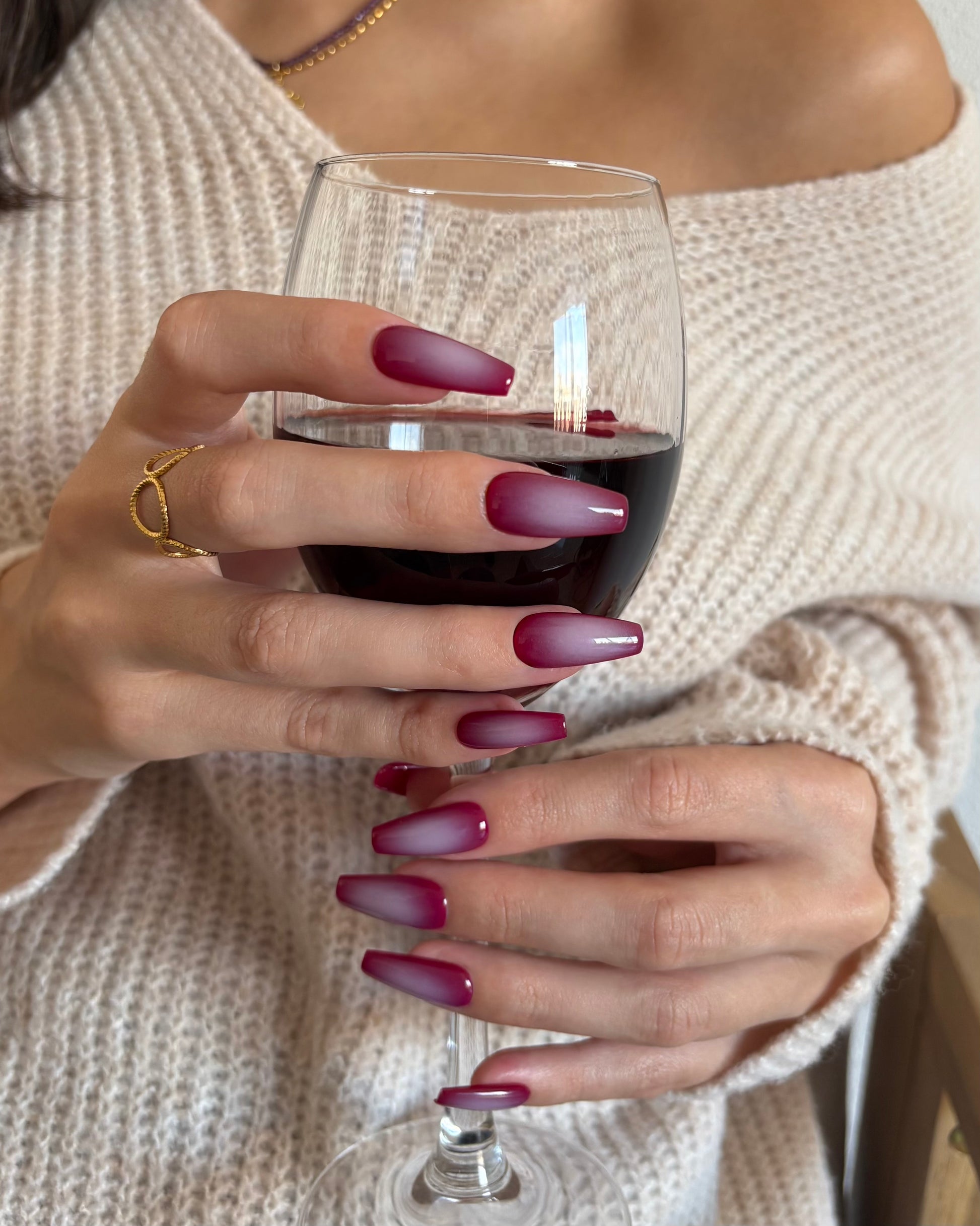set de uñas press-on burdeos con degradado aura en el centro de color beige hecho con aerógrafo  agarrando con  manos una copa de vino tinto
