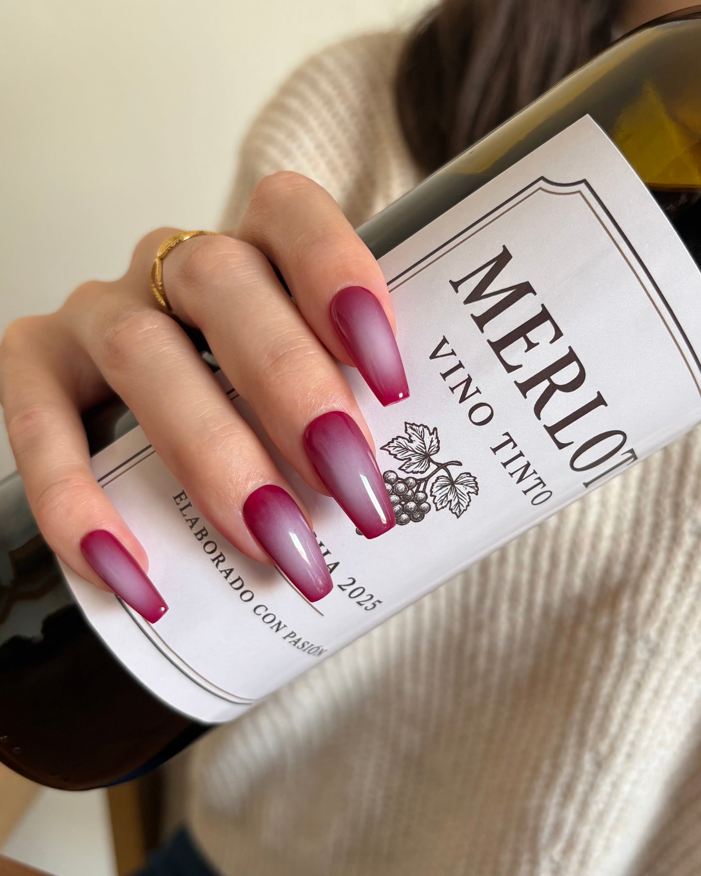 set de uñas press-on burdeos con degradado aura en el centro de color beige hecho con aerógrafo cogiendo una botella de vino merlot