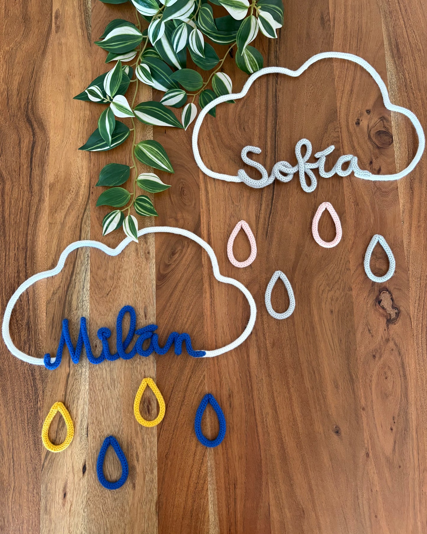dos móviles decorativos de nube con gotas y nombres personalizados con fondo madera y planta
